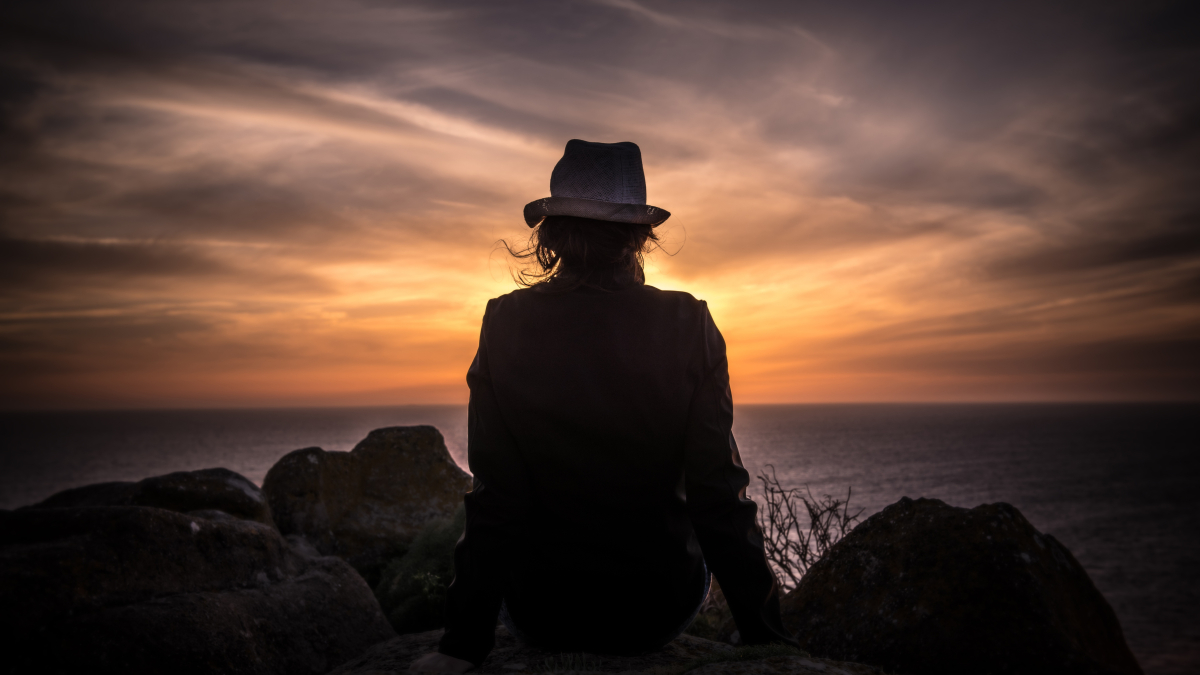Женщина сидит на горе и смотрит на закат