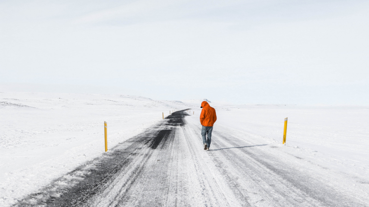Человек в красной куртке идет по зимней дороге