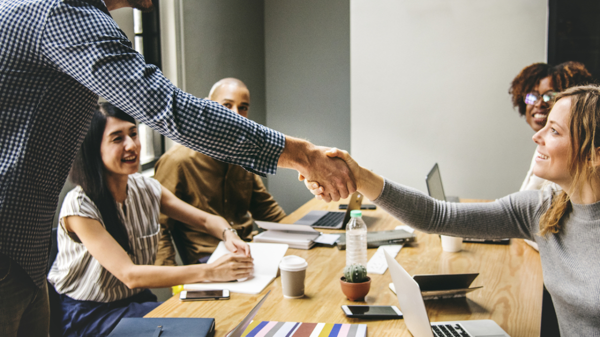Мужчина жмет руку женщине в компании коллег