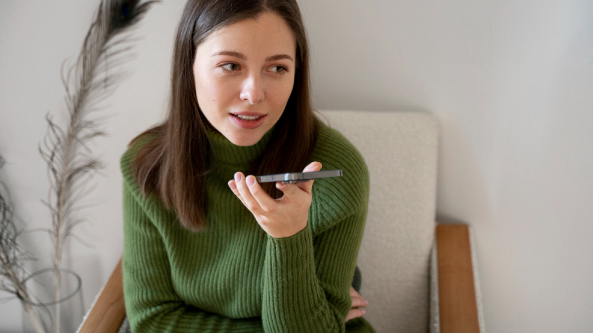 Девушка в зеленом свитере наговаривает сообщение по телефону.