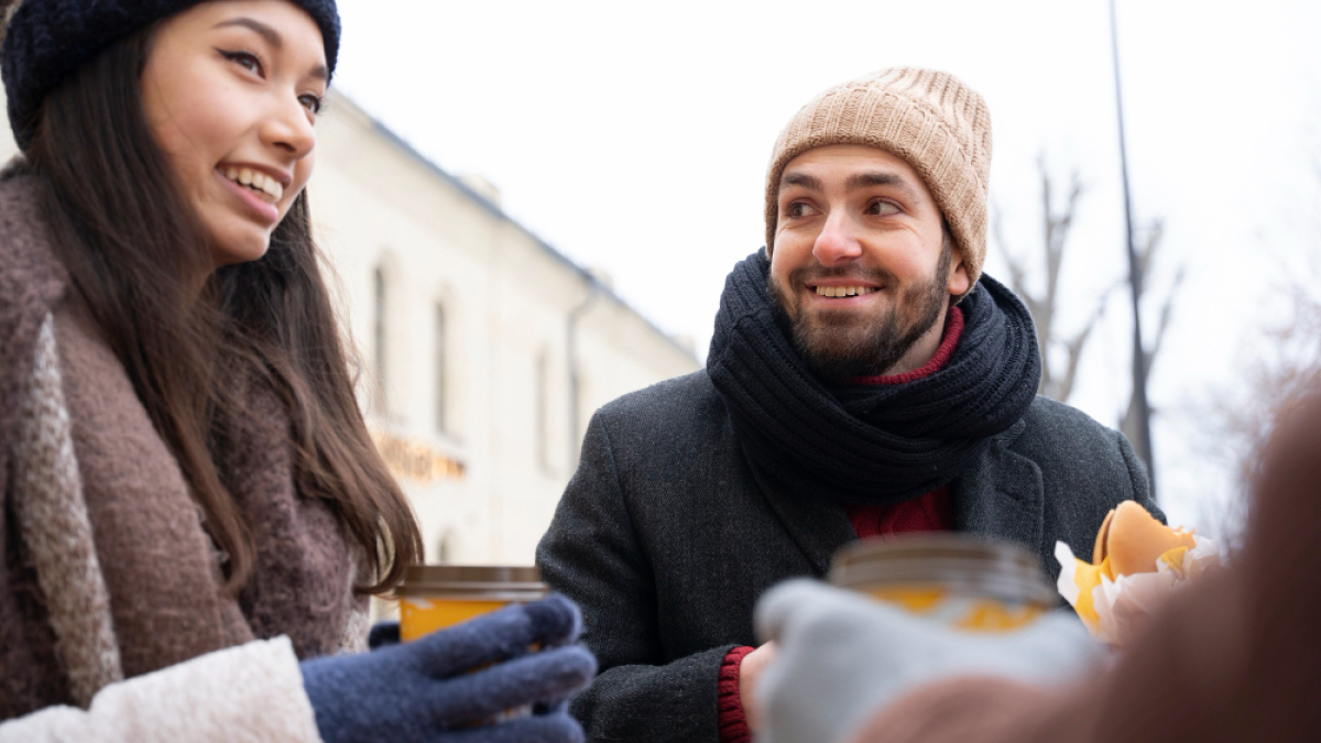 Люди в теплой одежде со стаканчиками в руках общаются зимой на улице
