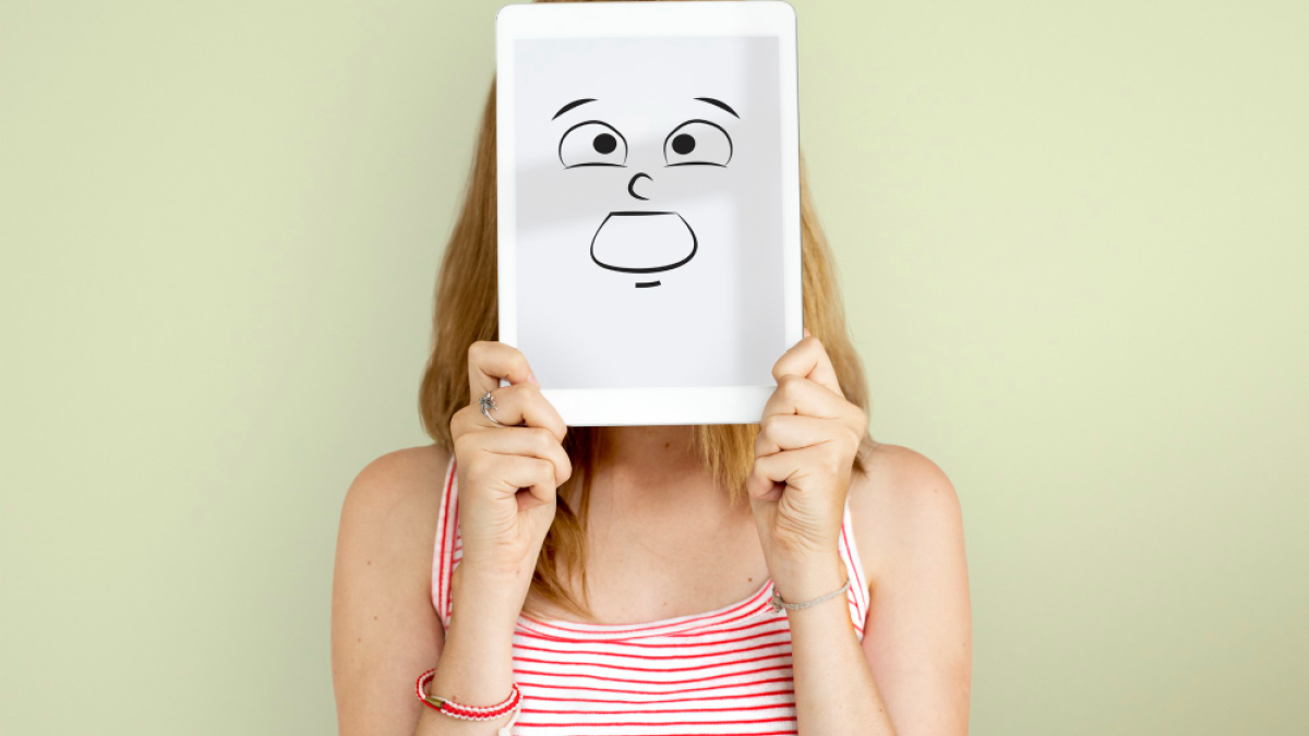 Девушка прячет лицо за картинкой с нарисованной эмоцией