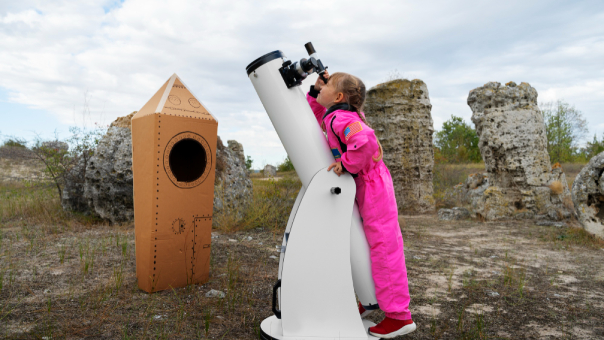 Девочка в розовом комбинезоне смотрит в телескоп на небо