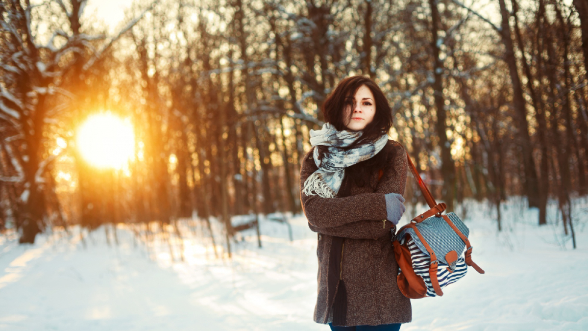 Девушка с рюкзаком позирует на фоне зимнего леса