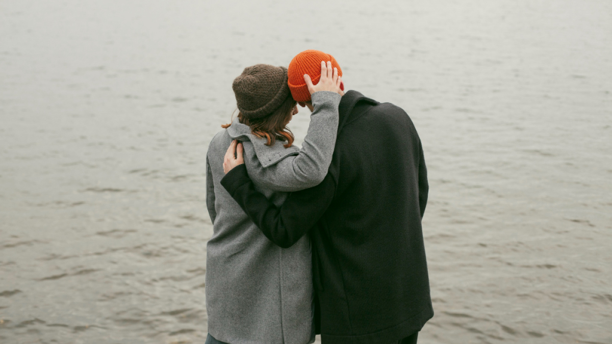 Пара стоит у воды и обнимается