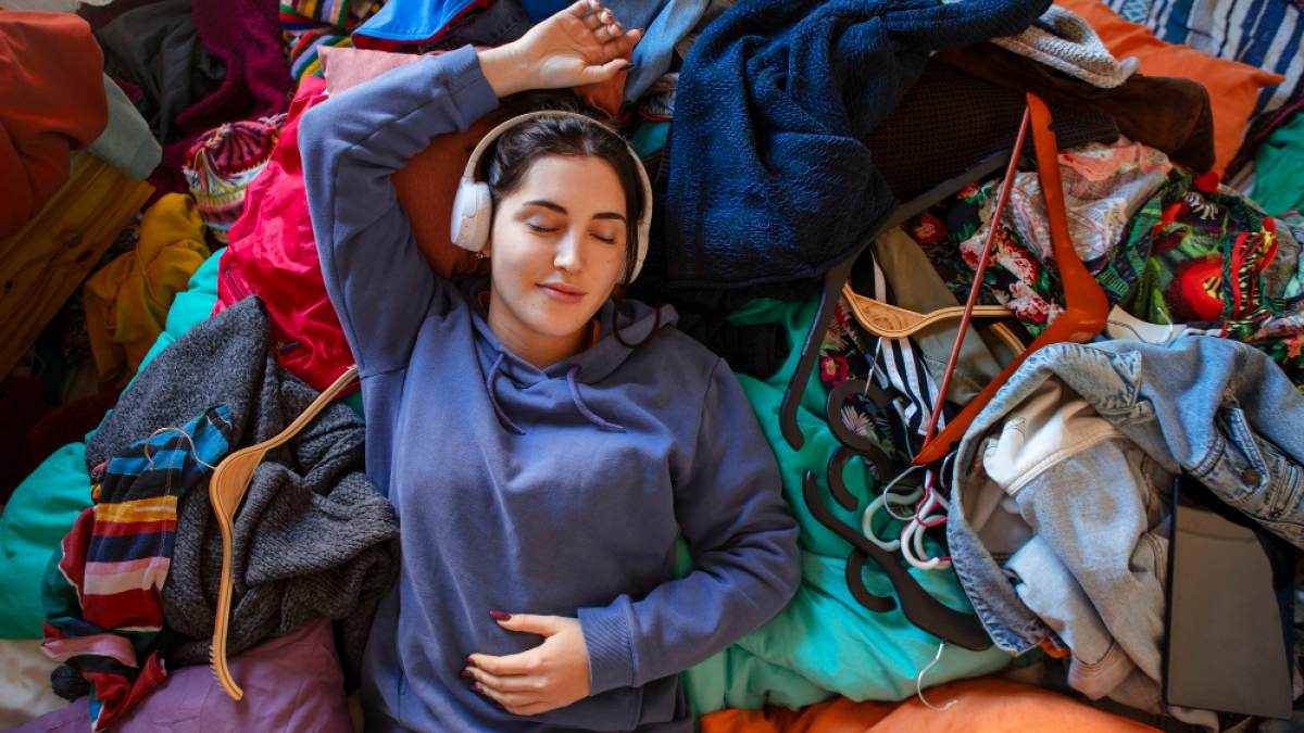 Девушка в наушниках слушает музыку на груде вещей.