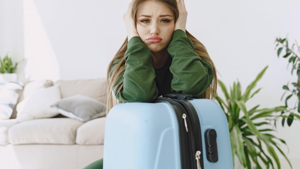 Девушка в зеленом свитере обнимает чемодан.