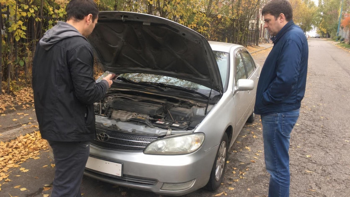 Мужчина осматривает подержанный автомобиль перед покупкой осенью