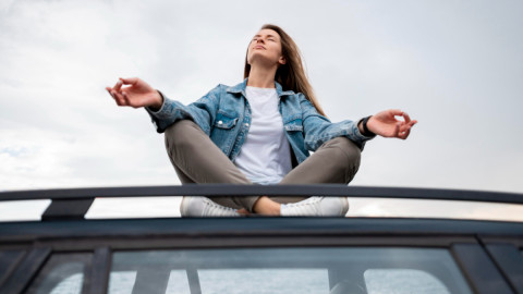 Девушка занимается йогой на крыше автомобиля на фоне неба