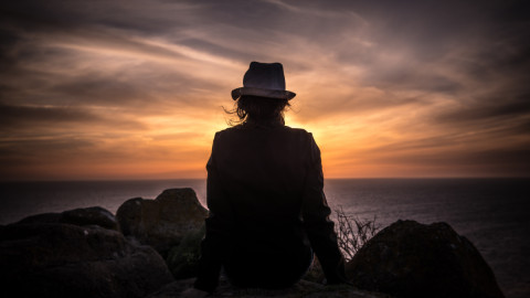 Женщина сидит на горе и смотрит на закат