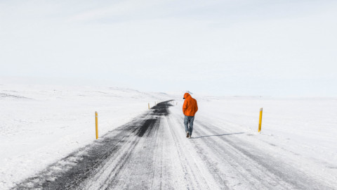 Человек в красной куртке идет по зимней дороге