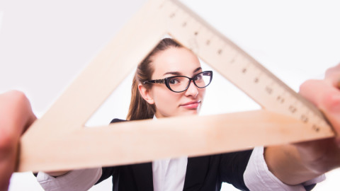 Девушка в офисном костюме и в очках держит перед собой линейку-треугольник