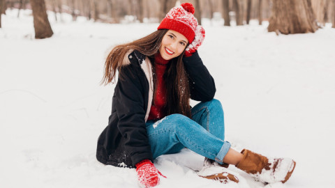 Девушка в красной шапке зимой сидит на снегу