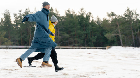 Мужчина и женщина в теплой одежде держатся за руку и бегут по снегу.