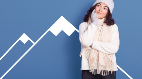 Девушка в свитере, шапке и шарфе стоит на фоне синей стены, на которой схематически нарисована гора