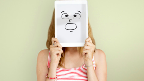 Девушка прячет лицо за картинкой с нарисованной эмоцией