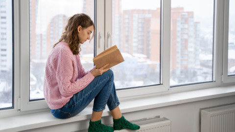 Женщина читает книгу возле окна