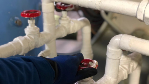 рука в перчатке поворачивает красный вентиль на белой трубе