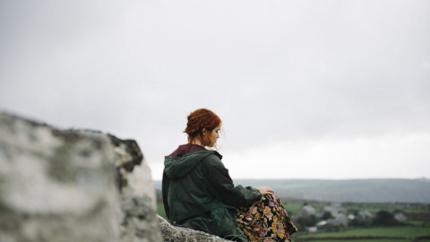 Девушка с рыжими волосами сидит на камнях и смотрит на долину