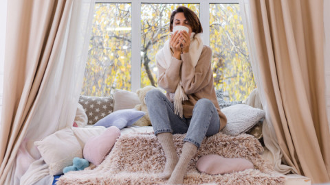 Девушка пьет чай дома, уютно устроившись на окне