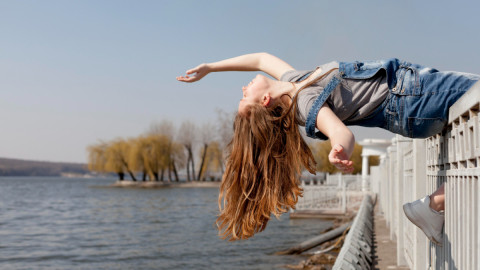 Рыжеволосая девушка склоняется над водой, сидя на ограде.