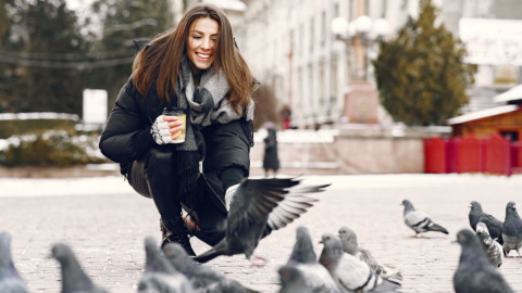 Девушка кормит голубей на площади весной.