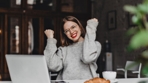 Девушка радуется удаче, сидя за столиком в кафе.