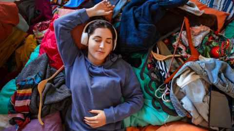 Девушка в наушниках слушает музыку на груде вещей.