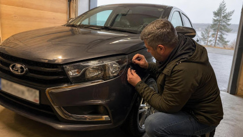 Мужчина закрашивает скол на кузове автомобиля в гараже осенью