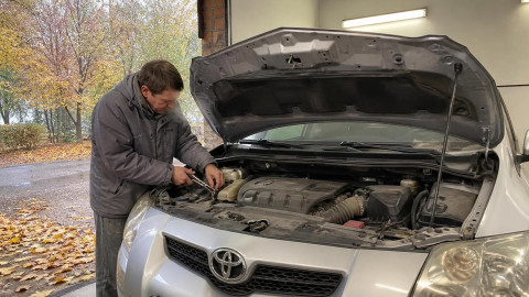 Мужчина промывает радиатор печки автомобиля под капотом осенью