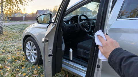 Водитель протирает резиновый уплотнитель двери автомобиля холодным октябрьским утром