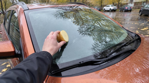 Мужчина натирает лобовое стекло автомобиля половинкой сырой картошки в октябре