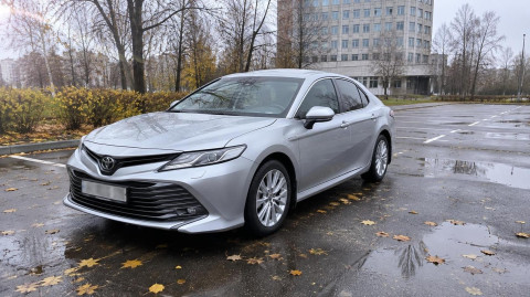 Серебристая Toyota Camry на мокрой площадке автосалона поздней осенью
